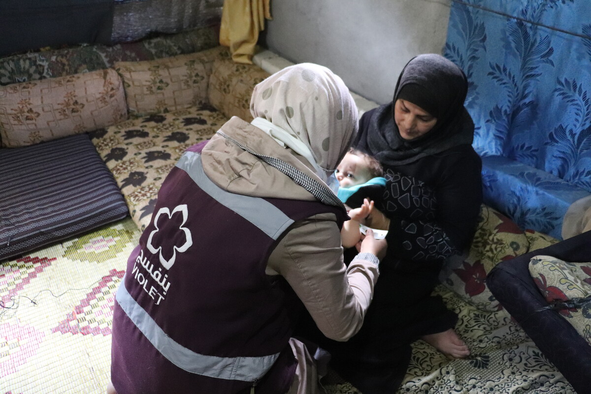 Syrian woman with a baby receiving help from a nurse